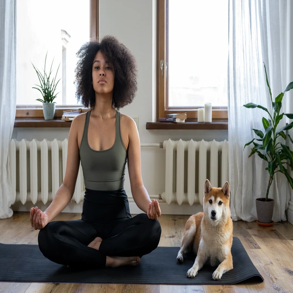 woman sitting on a mat in meditation with a dog next to her
